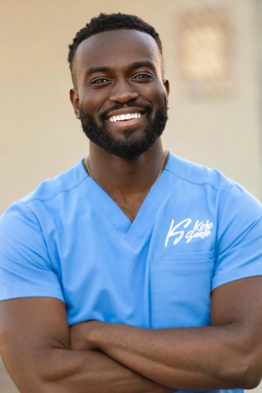 Dr. Kojo in light blue scrubs with arms crossed