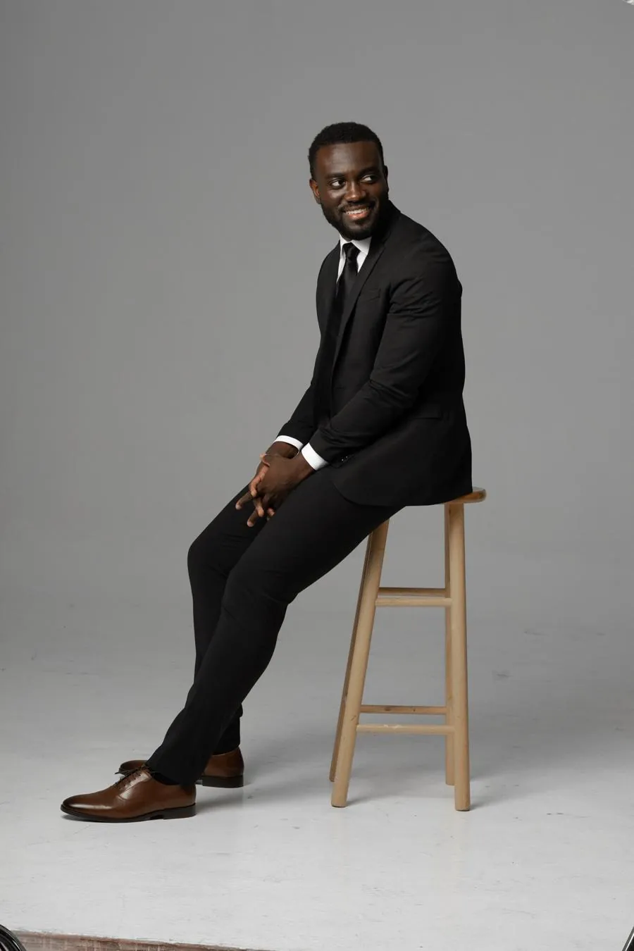 Dr. Kojo in a black suit on a wooden stool